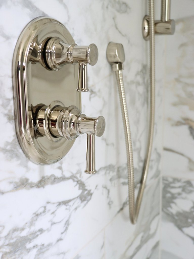 Polished nickel fixtures paired with warm tones in primary bathroom of custom home.