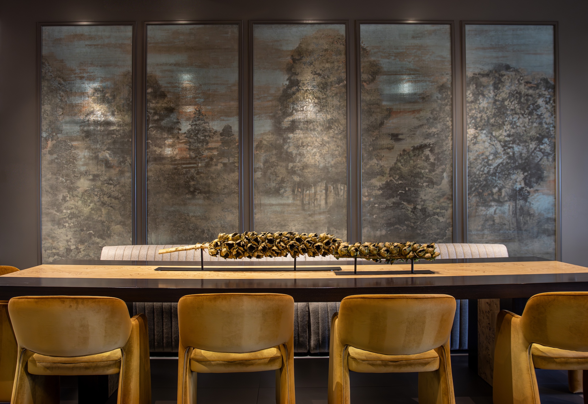 Unconventional luxury condo dining room in Omaha featuring Armoni silk wall coverings framed in custom millwork, gold velvet chairs, an elongated seating style, and an exotic wood table with a unique botanical centerpiece.